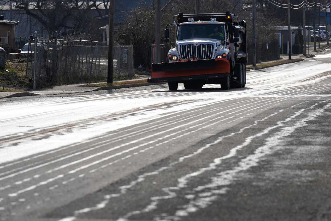 Un camion équipé d'un chasse-neige à l'avant applique de la saumure salée sur une route.