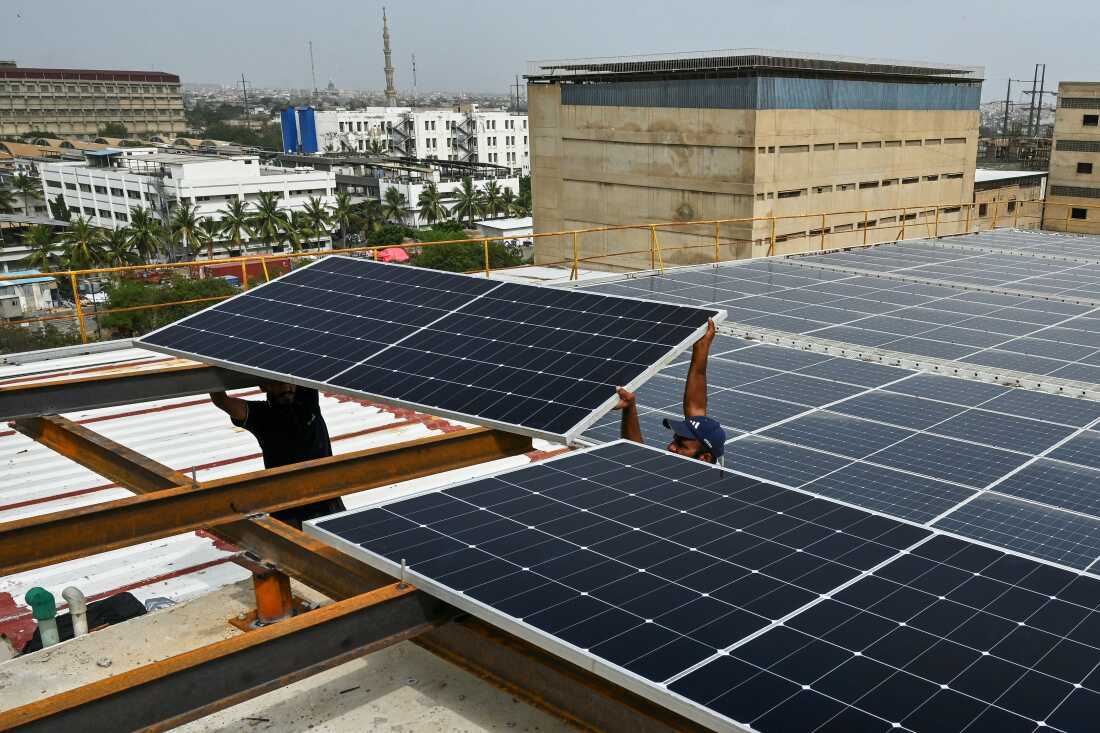 Sur cette photographie prise le 2 juillet 2025, des techniciens installent des panneaux solaires sur le toit d'une usine de la ville portuaire de Karachi, au Pakistan.
