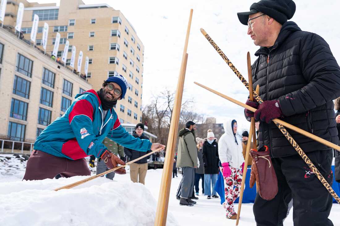 Bill Quackenbush de Ho-Chunk Nation, à droite, enseigne à Praneeth Kolli, à gauche, comment participer à la compétition de serpent des neiges lors du Frozen Assets Festival sur le lac Mendota, le samedi 7 février 2026, à Madison, Wisconsin. Le serpent des neiges est un sport d'hiver autochtone traditionnel dans lequel les joueurs glissent des bâtons de bois fabriqués à la main dans une tranchée faite de neige pour parcourir de longues distances. Photo de Kayla Wolf