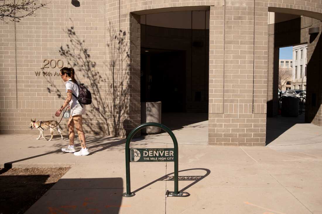 Une femme promène son chien devant le bâtiment des élections de Denver, fait de briques brunes.