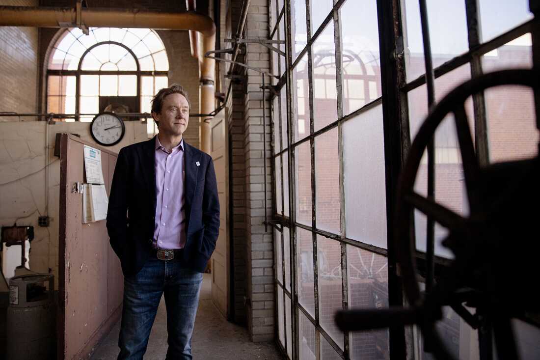 Le maire de Denver, Mike Johnston, se trouve à l'intérieur de la chaudière Cherokee, à côté d'une grande et grande fenêtre composée d'une grille de carreaux carrés.
