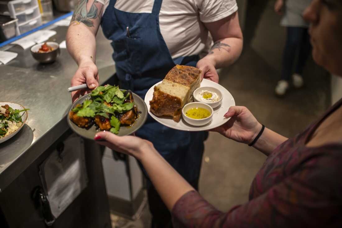 Un chef remet à un serveur des plats de nourriture à emporter à table, notamment de gros morceaux de pain trempés dans de l'huile.