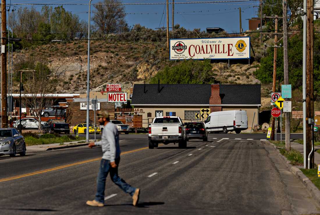 Un homme traverse une rue d'une ville avec un panneau publicitaire qui dit "Bienvenue à Coalville" à flanc de colline au bout de la rue. 
