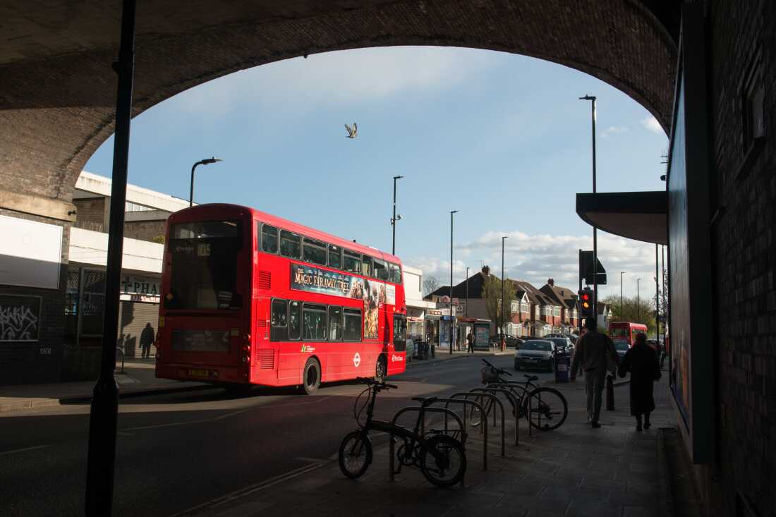 Un bus rouge à impériale passe sous une arche de pont ferroviaire à la station de métro Greenford.