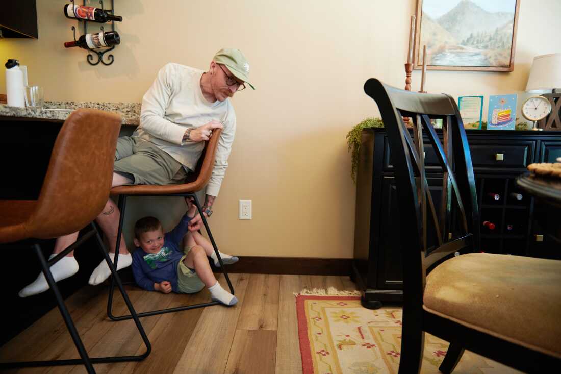 Neil Petersen est assis sur une chaise pendant que Jack, 4 ans, joue sous lui. 
