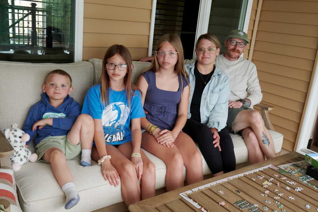 Jack Petersen, 4 ans, Eden Svejda, 11 ans, Piper Svejda, 12 ans, Amber Petersen et Neil Petersen posent pour un portrait de famille à Iowa City, Iowa, le dimanche 14 juin 2026. La famille vit à Mason City, Iowa et rendait visite aux parents d'Amber pour le week-end. (Cliff Jette pour NPR)