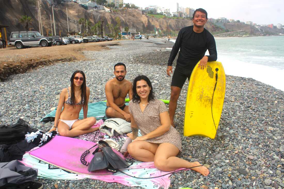 Cette photo montre Fabricia Laura à Redondo Beach à Lima, au Pérou, avec trois amis. Elle et deux de ses amis, un homme et une femme en maillot de bain, sont assis sur des serviettes étalées sur une plage constituée de gros galets gris. Le troisième ami, un homme, se tient à côté d’eux, avec un bodyboard jaune. L'océan Pacifique se trouve sur le côté droit du cadre.