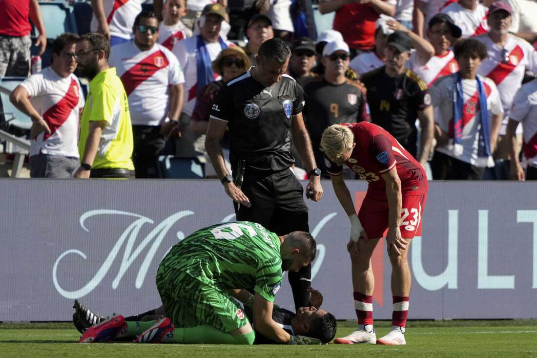 Sur cette photo de juin 2024, l'arbitre assistant Humberto Panjoj est allongé sur le dos sur un terrain de football vert après s'être évanoui lors d'un match de football professionnel de la Copa América à Kansas City, Kansas. Un footballeur en uniforme vert est agenouillé par terre à côté de lui. Un autre footballeur, en rouge, et un arbitre, en noir, se tiennent à côté de Panjoj et le regardent.