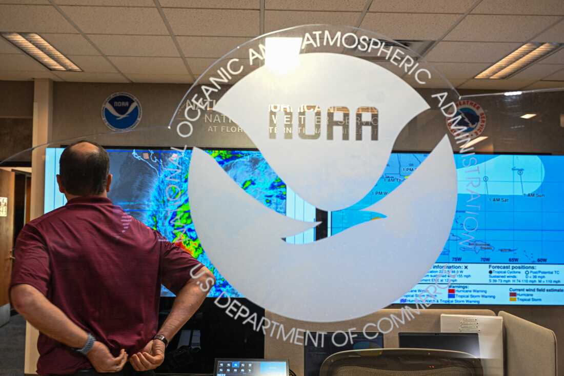 Un employé, dos à la caméra, regarde plusieurs modèles d'ouragans affichés sur de grands écrans au National Hurricane Center de la National Oceanic and Atmospheric Administration à Miami, le 30 mai 2025.
