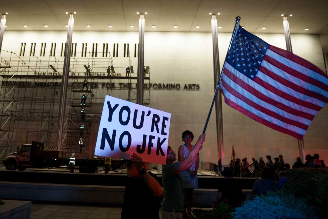 Les manifestants brandissent un drapeau américain et signent alors que les travailleurs se préparent à retirer le nom du président Donald Trump du John F. Kennedy Center for the Performing Arts à Washington, le samedi 13 juin 2026.