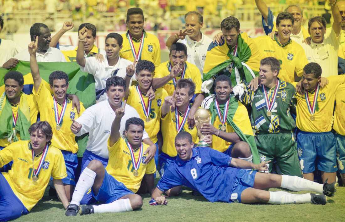 Les joueurs de l'équipe de football du Brésil posent pour une photo de groupe après avoir remporté la finale de la Coupe du Monde de la FIFA 1994 au stade Rose Bowl de Pasadena, en Californie, en juillet 1994. La plupart des joueurs portent des maillots jaunes et beaucoup ont le bras levé pour célébrer.