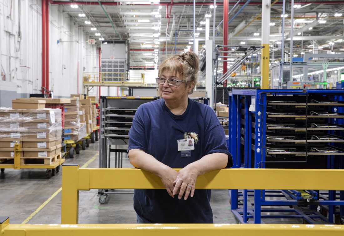 Doris Hamby se tient dans l'usine. Elle porte un T-shirt bleu marine et des lunettes.
