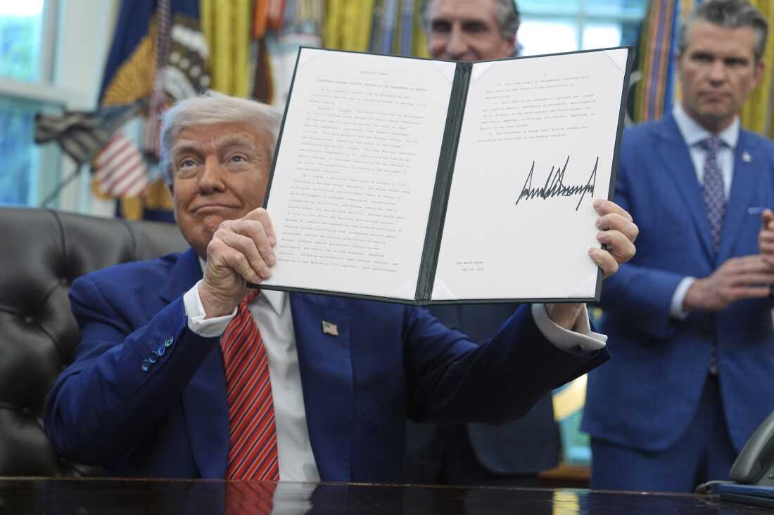 Sur cette photo, le président Trump brandit un décret qu'il a signé. Il est assis à un bureau du bureau ovale de la Maison Blanche le 23 mai 2025.