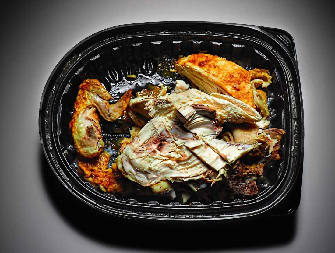 Cette photo montre un plat de poulet partiellement mangé dans un contenant à emporter en plastique noir.