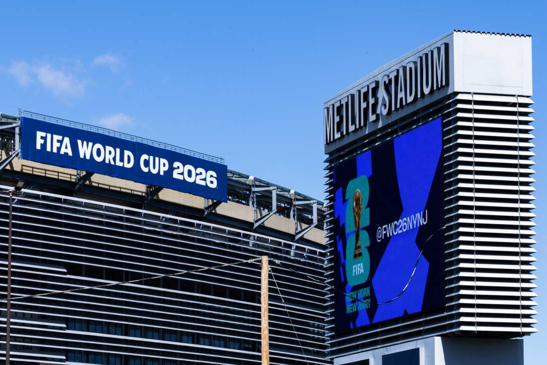 Cette photo montre l'extérieur du stade MetLife à East Rutherford, New Jersey. Une banderole bleue placée au sommet du stade indique : "COUPE DU MONDE FIFA 2026."