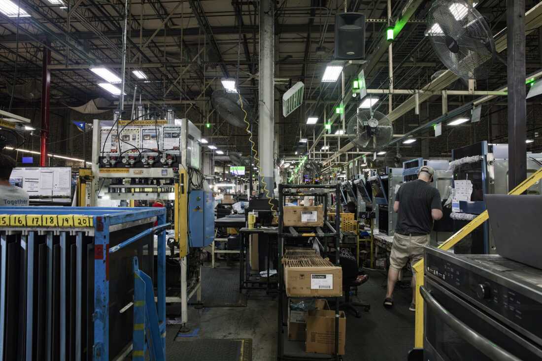 Un ouvrier à la chaîne de montage installe des pièces sur un four dans une grande usine.