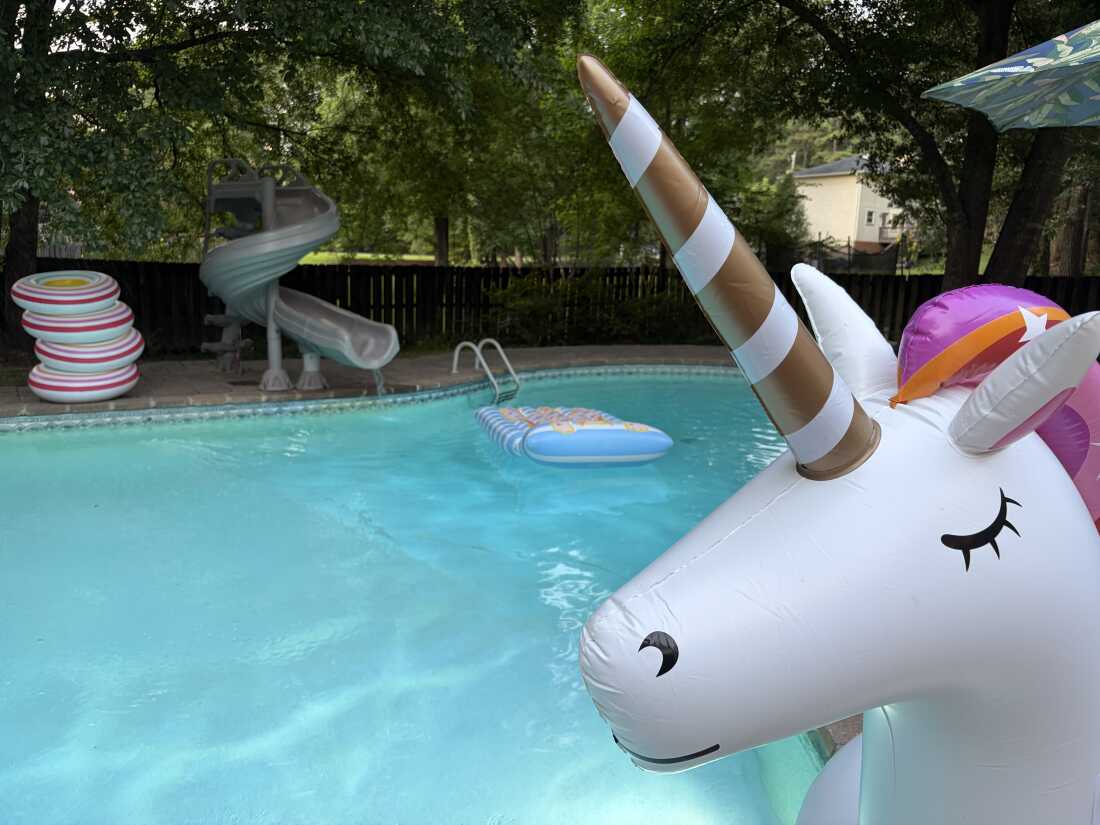 Une piscine avec toboggan et licorne gonflable, radeau et bouées.