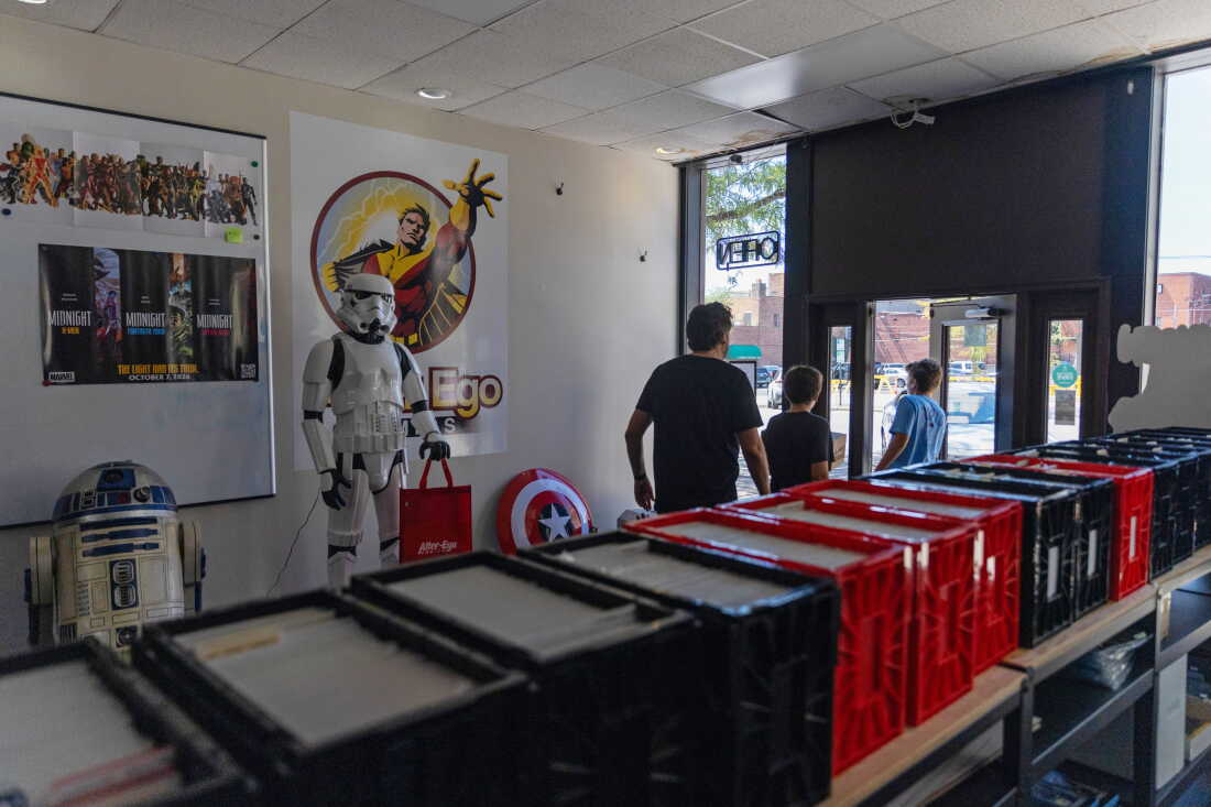Un homme et deux garçons passent devant des modèles grandeur nature de R2-D2 et d'un Stormtrooper de Star Wars alors qu'ils sortent du magasin.