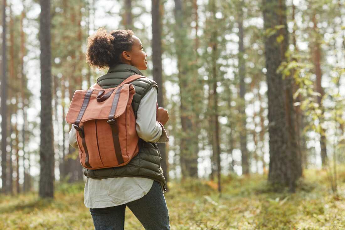 Une photo d'archive d'une jeune femme noire portant un sac à dos aime faire de la randonnée dans une forêt.