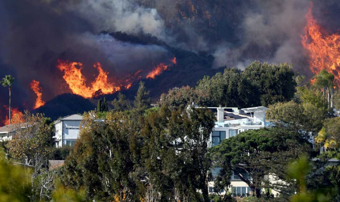 Un incendie qui fait rage derrière une rangée de maisons dégage une fumée noire.
