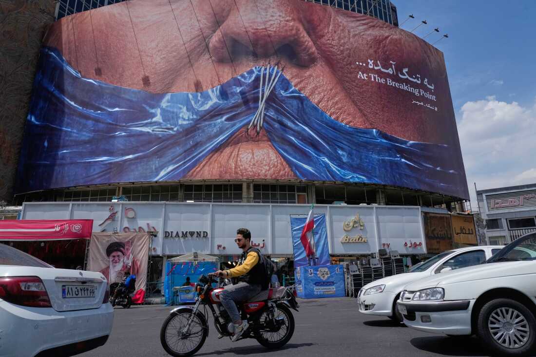 Des véhicules passent devant un panneau publicitaire avec une illustration montrant le détroit d’Ormuz et les lèvres cousues du président Trump sur une place du centre-ville de Téhéran, en Iran, le 2 mai.
