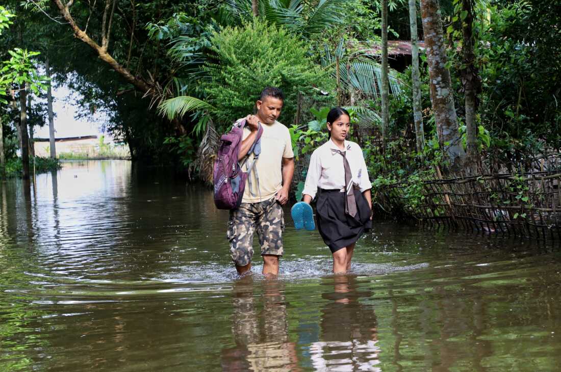 Une écolière et son père traversent les eaux de crue dans le village d'Alengmora à Jorhat, en Inde, le lundi 10 août 2026.