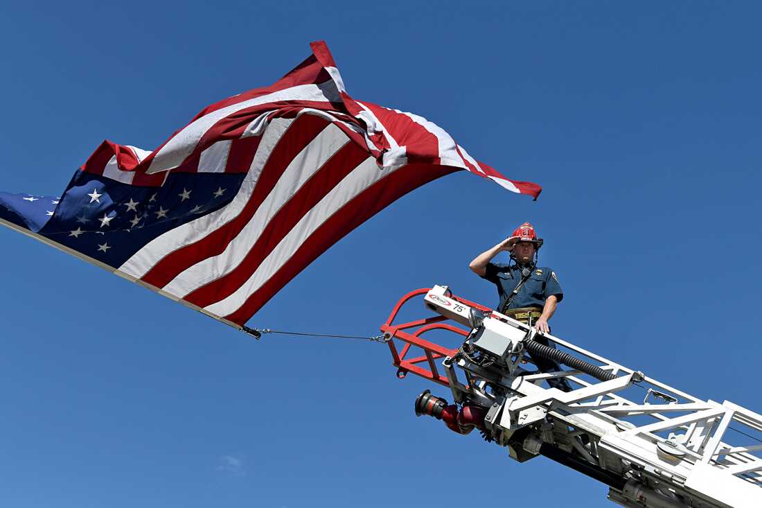 Un capitaine du district de protection contre les incendies de Clifton salue le cortège qui transporte les corps de trois pompiers tués alors qu'ils combattaient l'incendie de Snyder à Grand Junction, au Colorado, le 28 juin. Il est au sommet d'une échelle sur un camion de pompiers et un drapeau américain flotte au-dessus de lui.
