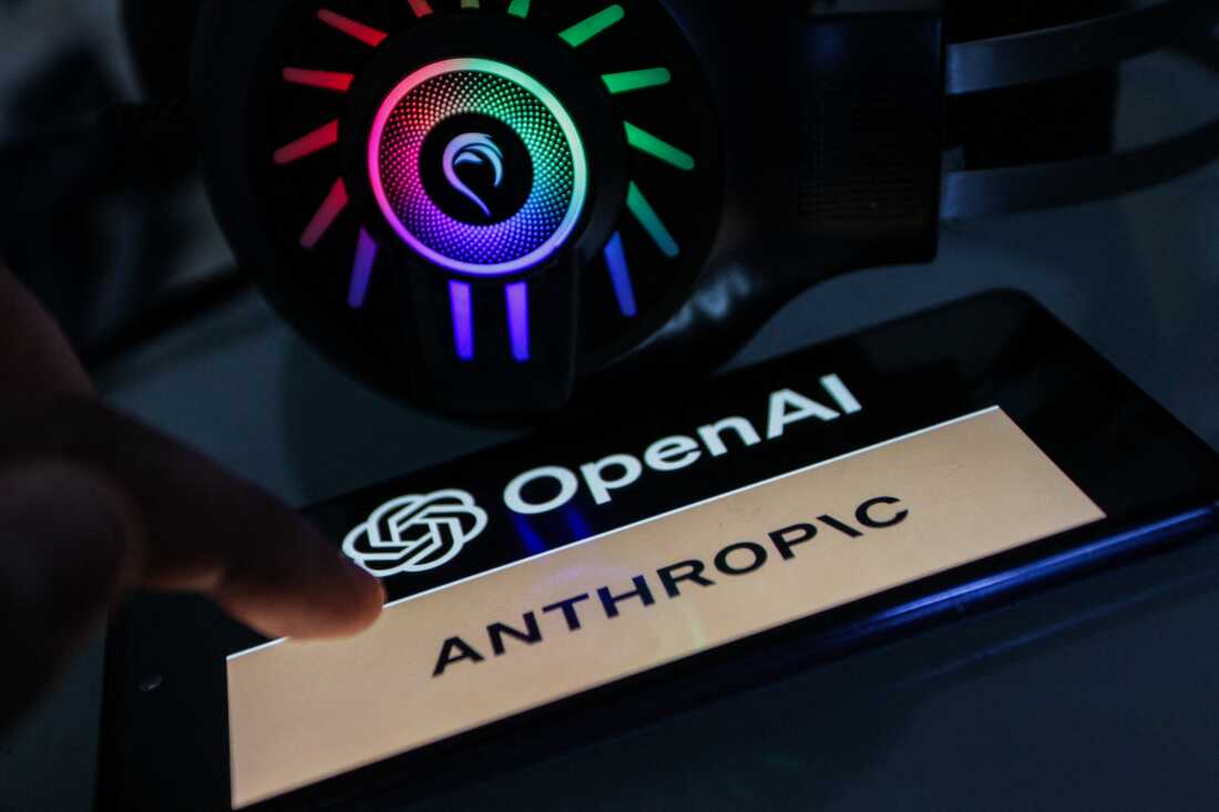 Un smartphone affichant le logo OpenAI au-dessus du mot "Anthropique" est vu à côté d’un casque allumé.