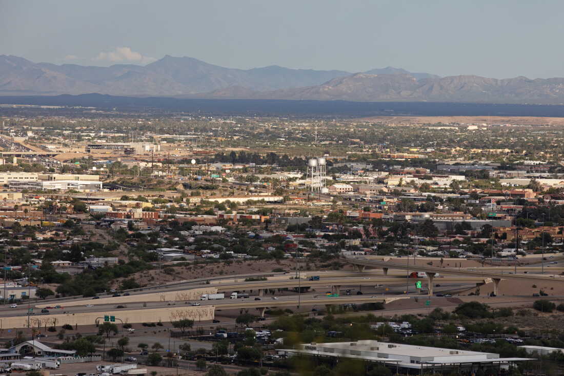 Cette photo montre une vue panoramique de Tucson, en Arizona, avec ses bâtiments et ses autoroutes. Les montagnes s'élèvent en arrière-plan.