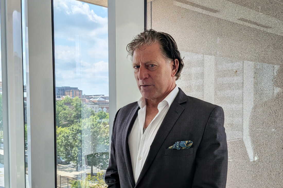 Richardson porte un costume sombre et une chemise blanche partiellement déboutonnée.
