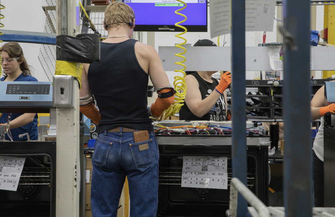 Au moins cinq personnes travaillent sur une chaîne d'assemblage manipulant des composants électroniques.