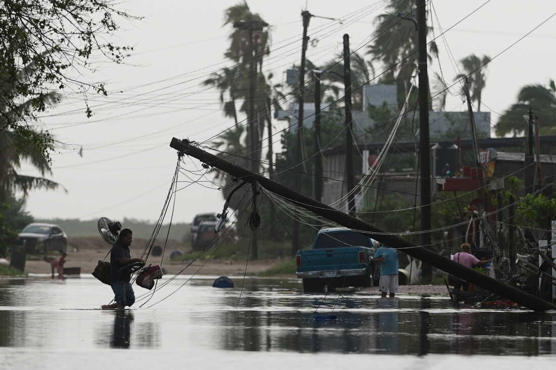 Un homme transporte des objets à travers les eaux de crue devant des lignes électriques tombées après le passage de l'ouragan Polo à Puerto San Carlos, dans l'État de Baja California Sur, au Mexique, le mardi 29 septembre 2026.