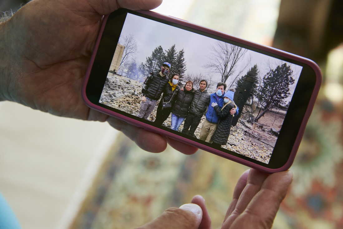 Louie Delaware tient son téléphone montrant une photo de sa famille à l'extérieur de leur maison incendiée après l'incendie de Marshall, qui a détruit plus de 1,100 maisons à Louisville, Superior et dans le comté non constitué de Boulder. Les incendies de forêt font partie des impacts liés au climat au centre du procès du comté de Boulder contre ExxonMobil et Suncor Energy. (Jimena Peck pour Radio Nationale Publique)