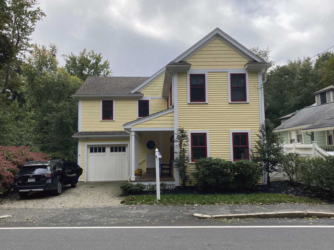 Une maison jaune à plusieurs étages avec un garage et une allée.