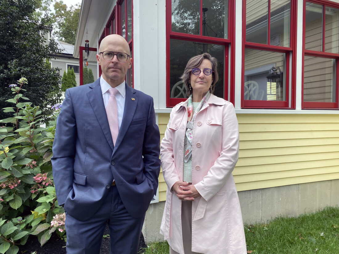 Adam Chapdelaine et Jill Hai se tiennent devant une maison aux planches à clin jaunes et aux fenêtres encadrées de rouge.