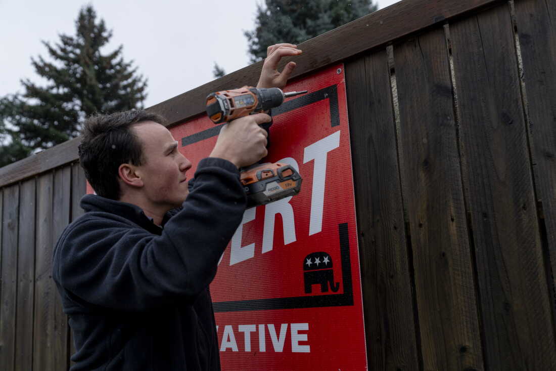 Le représentant de l'État du Montana, Lukas Schubert, utilise une perceuse pour accrocher un panneau de campagne sur une clôture en bois à Kalispell.