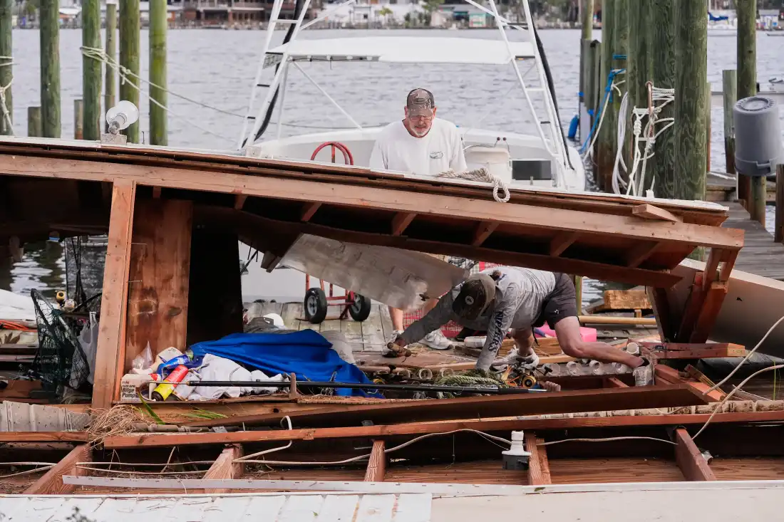 Des gens récupèrent leurs affaires dans un hangar à bateaux effondré à la suite de l'ouragan Isaias à Destin, en Floride, le samedi 10 octobre 2026. (AP Photo/Gerald Herbert)