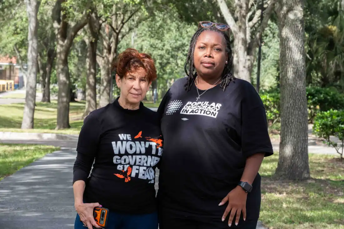 Les bénévoles de Florida Rising, Maggie Fernandez, 68 ans (à gauche) et Tia Bell-Williams, 55 ans, se tiennent ensemble dans une zone bordée d'arbres. Fernandez porte un t-shirt noir qui dit "Nous ne serons pas gouvernés par la peur" et Bell-Williams porte un t-shirt noir qui dit "La démocratie populaire en action."