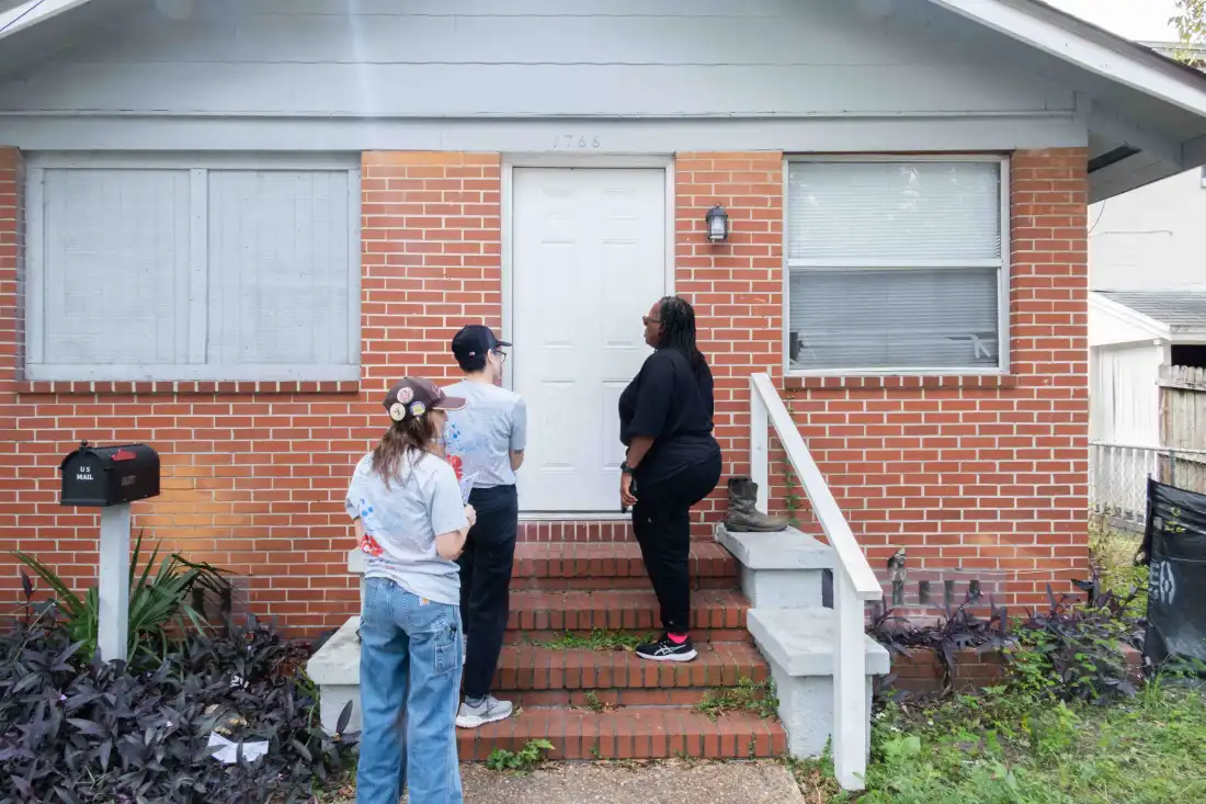 Trois volontaires de Florida Rising se tiennent devant la porte d'entrée d'une maison en brique à Jacksonville, en Floride.
