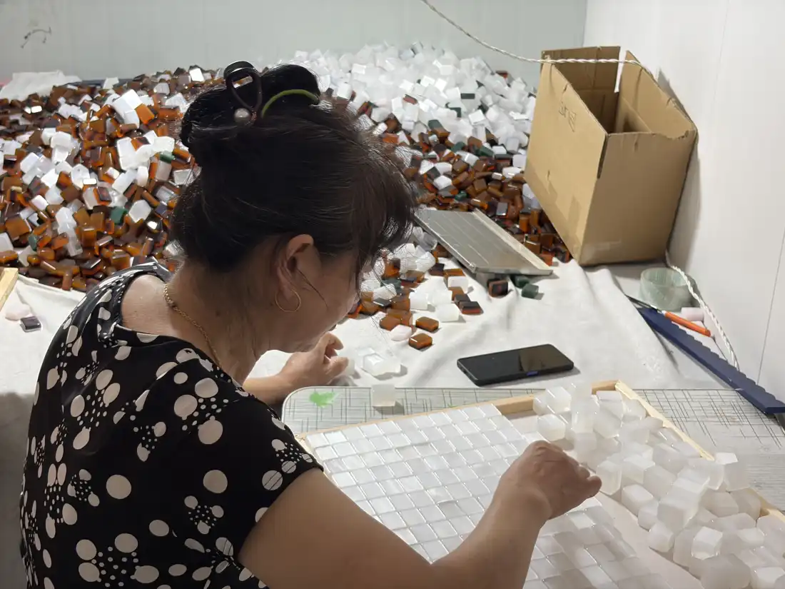 Une femme inspecte les carreaux blanc perle et orange brûlé pour s’assurer qu’il n’y a pas d’imperfections.