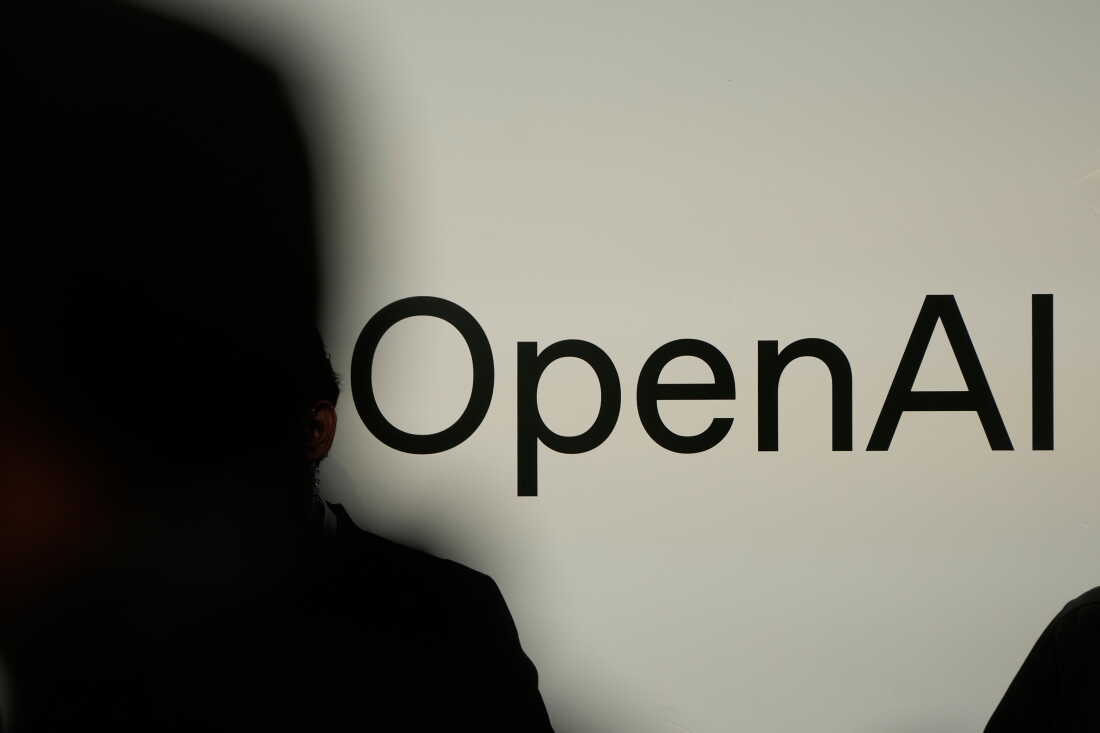 Une personne en silhouette se tient devant un écran affichant le logo d'OpenAI.